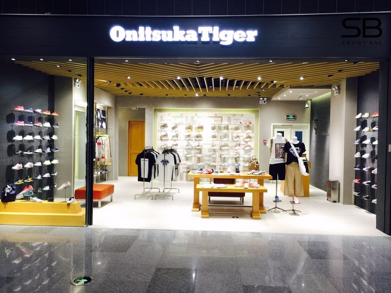 Ảnh chụp mặt tiền một cửa hàng Onitsuka Tiger chính hãng, với logo thương hiệu nổi bật và cửa kính s