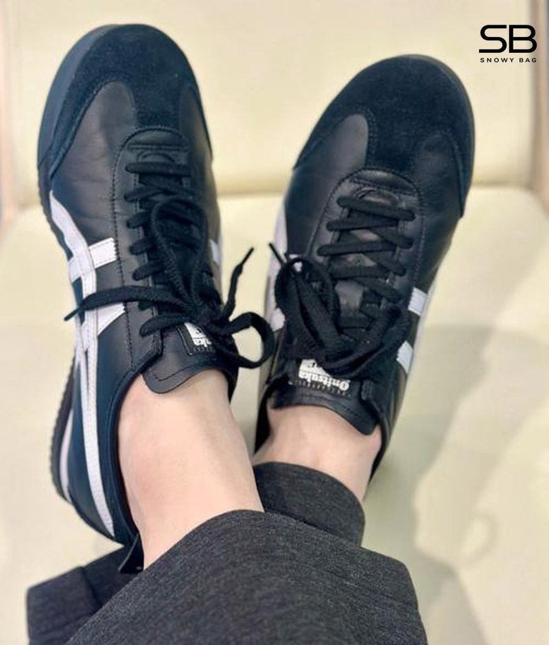 Một khách hàng đang thử giày Onitsuka Tiger tại cửa hàng, với nhân viên hỗ trợ và gương để soi chân.